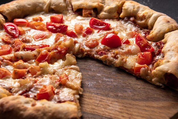 Close up of tasty sliced pizza with tomatoes and herbs without one slice over wooden table backgroun