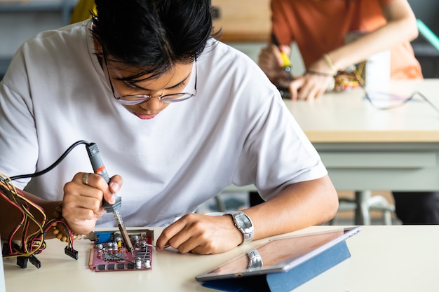 Close up of teen asian boy in electronics class working on a project alone. Education concept.