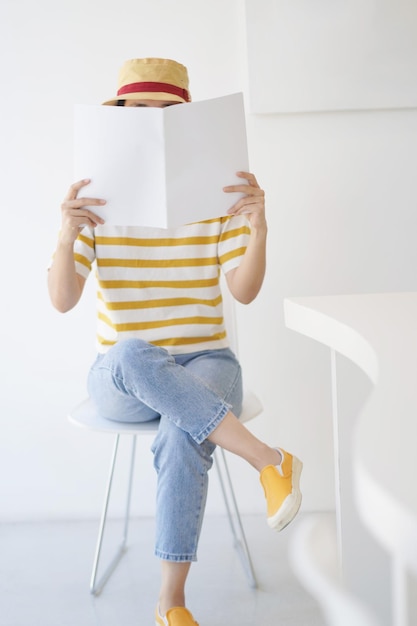 Close up teenage girl holding and reading book or magazine with white wall in copy space concept