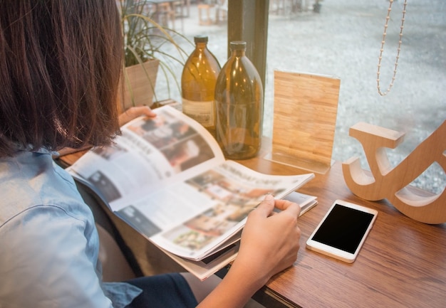 Close up teenage girl holding and reading magazine at cafe