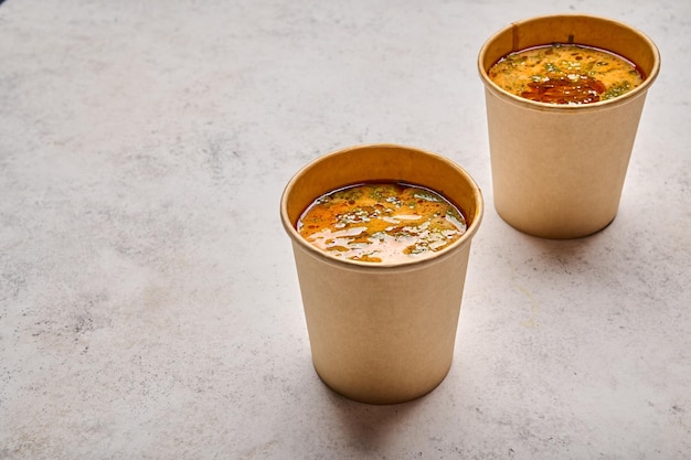 Close up tom yam soup with salmon and seafood in two paper solid containers on light background