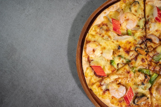 Close up top view of tasty hot baked seafood crispy pizza mussels shrimps and kani with chili pepper and melted mozzarella cheese on round pizza dough on a wooden pizza pan over concrete texture