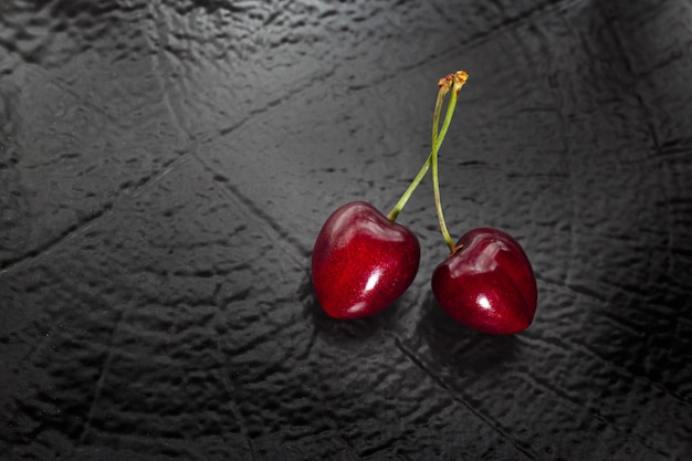 Close-up top view of two heart-shaped red cherries on black textured background with copy-space