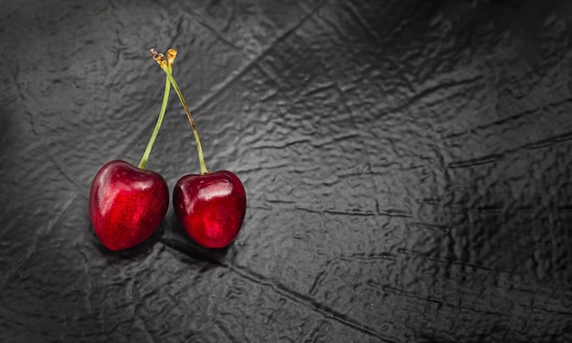 Close-up top view of two heart-shaped red cherries on black textured background with copy-space