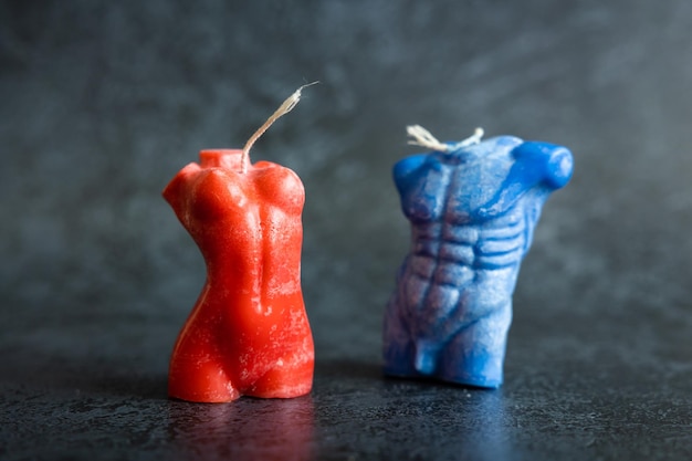 Close up of two handmade candles from soy wax in shape man torso and woman body isolated on dark background