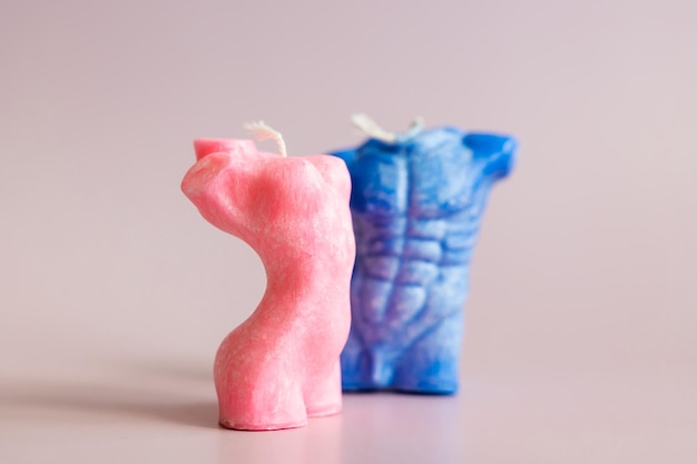 Close up of two handmade candles from soy wax in shape man torso and woman body isolated on pastel background