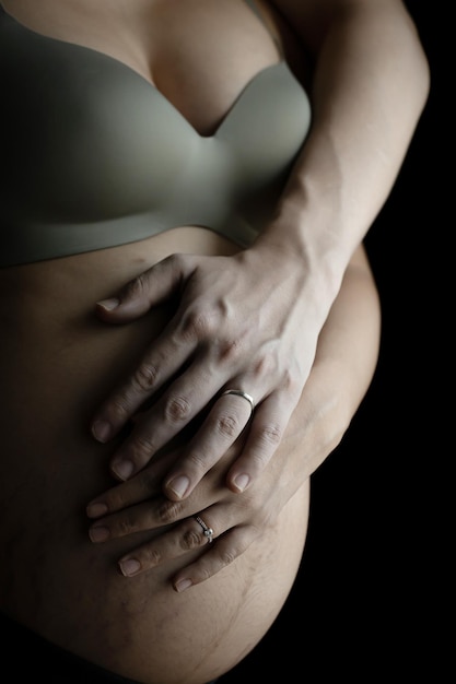 Close up of two hands wearing wedding rings on pregnant woman touching her big belly