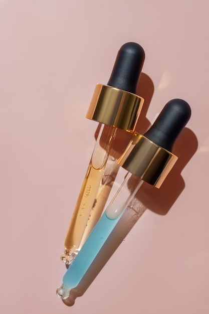 Close up of two pipettes with pouring liquid serum and shadows on beige background Trendy cosmetics shot with hard shadows