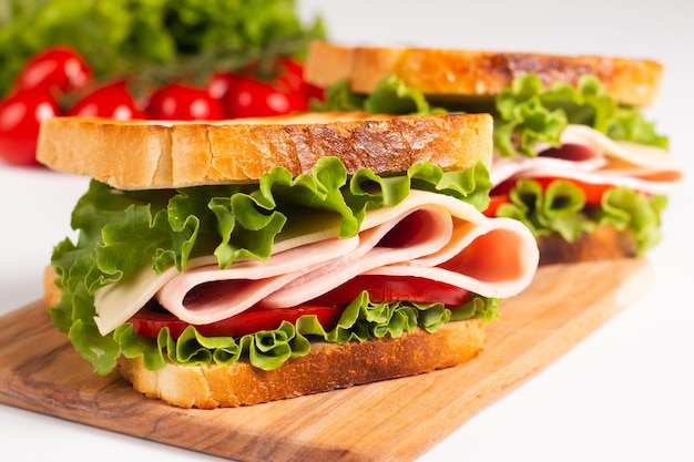 Close-up of two toasted sandwiches with fresh ham, cheese and vegetables on background.