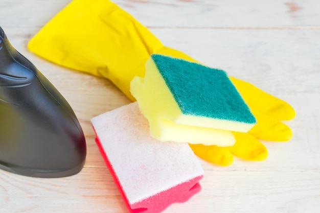 Close up of twoo clening sponges yellow rubber gloves and black plastic spray bottle of detergent on wooden background