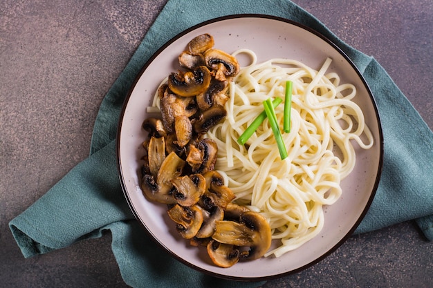 Close up of udon noodles and fried mushrooms on a plate for homemade dinner top view