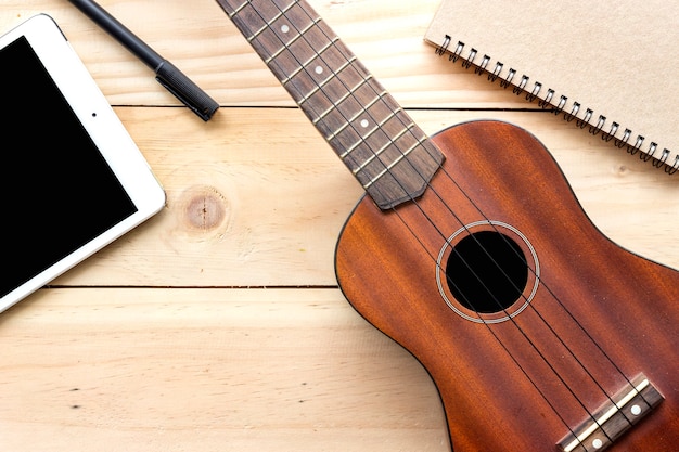 close-up ukulele, tablet computer and notebook on wood background. over light