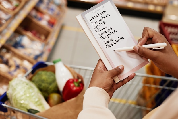 Close up of unrecognizable African-American woman holding shopping list while buying food in supermarket, copy space