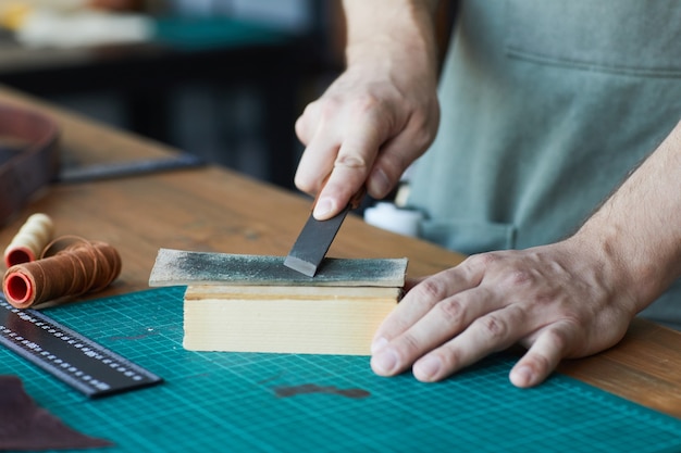 Close up of unrecognizable male artisan working with leather in workshop studio small business conce...