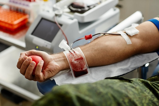 Close up of unrecognizable male donor donating blood and squeezing stress ball copy space