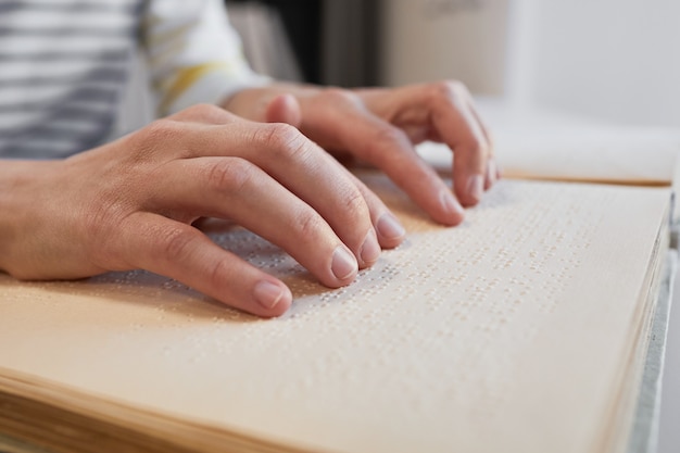 Close up of unrecognizable man reading braille book in college library copy space