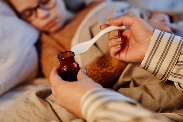 Close up of unrecognizable mother giving medicine to sick child recovering at home copy space