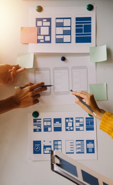 Close up ux developer and ui designer brainstorming about mobile app interface wireframe design on table with customer breif and color code at modern officeCreative digital development agency