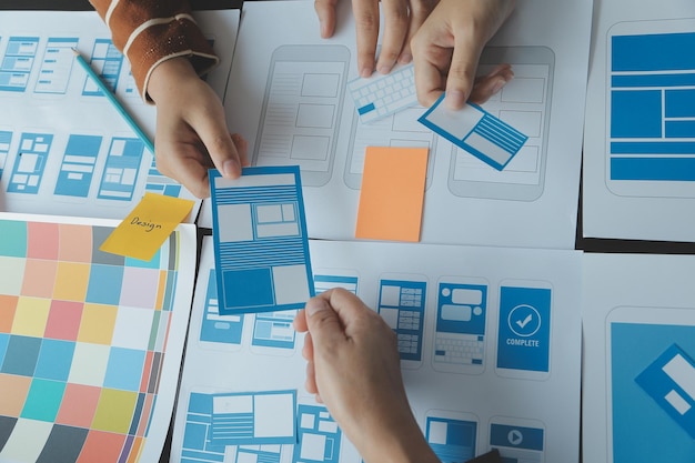 Close up ux developer and ui designer brainstorming about mobile app interface wireframe design on table with customer breif and color code at modern officeCreative digital development agency