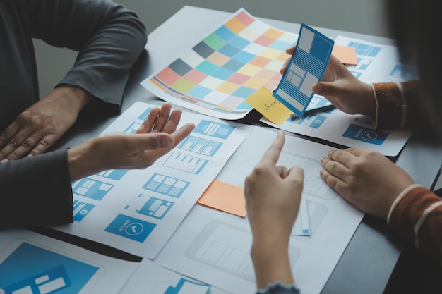 Close up ux developer and ui designer brainstorming about mobile app interface wireframe design on table with customer breif and color code at modern officeCreative digital development agency