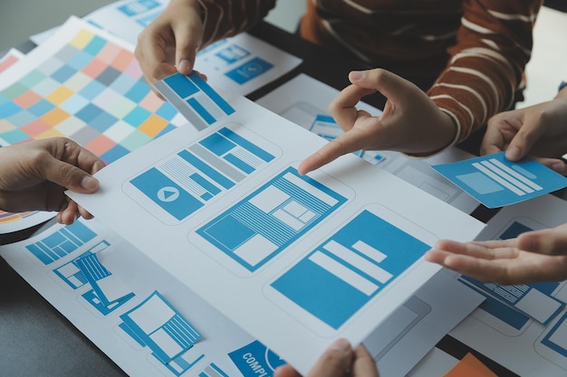 Close up ux developer and ui designer brainstorming about mobile app interface wireframe design on table with customer breif and color code at modern officeCreative digital development agency