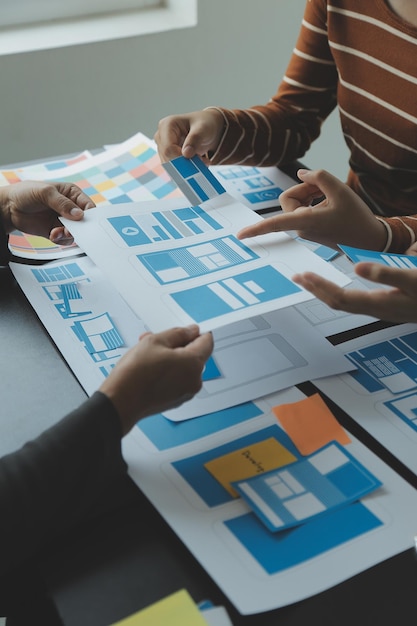 Close up ux developer and ui designer brainstorming about mobile app interface wireframe design on table with customer breif and color code at modern officeCreative digital development agency