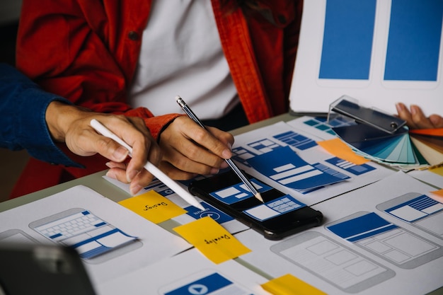 Close up ux developer and ui designer brainstorming about mobile app interface wireframe design on table with customer breif and color code at modern officeCreative digital development agency