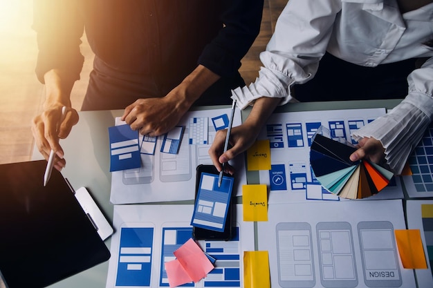 Close up ux developer and ui designer brainstorming about mobile app interface wireframe design on table with customer breif and color code at modern officeCreative digital development agency