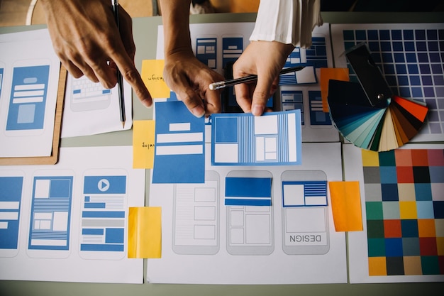 Close up ux developer and ui designer brainstorming about mobile app interface wireframe design on table with customer breif and color code at modern officeCreative digital development agency