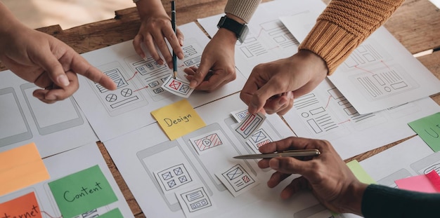 Close up ux developer and ui designer brainstorming about mobile app interface wireframe design on table with customer breif and color code at modern officeCreative digital development agency