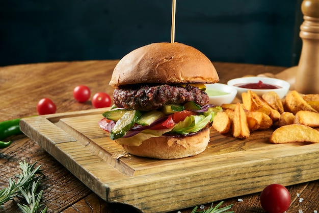 Close up view on burger with french fries on craft brown paper. Traditional fast food. fresh tasty hamburger with lettuce, tomato, cheese and cucumber. Copy space for design. Unhealthy food. Fat