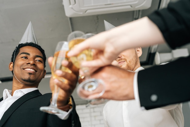 Close-up view of business team of multinational employees holding clinking glasses of champagne and smiling cheerfully at corporate New Year or Happy Christmas eve.