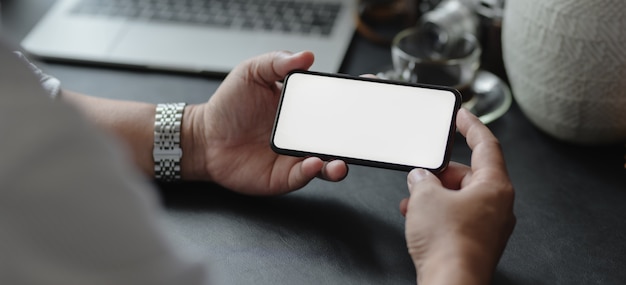 Close-up view of businessman holding blank screen smartphone in his modern office room 