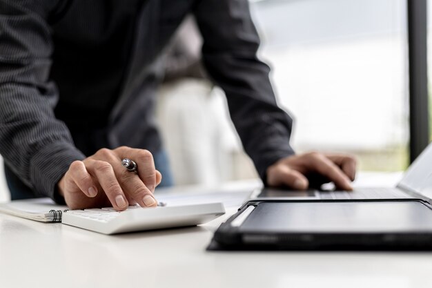 Close-up view A businessman using a calculator to calculate numbers on a company's financial documents, he is analyzing historical financial data to plan how to grow the company. Financial concept.