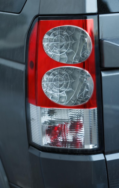 Close up view of a cars tail light The tail light is red and clear featuring intricate internal designs visible through the transparent sections It is mounted on the rear side of a grey car