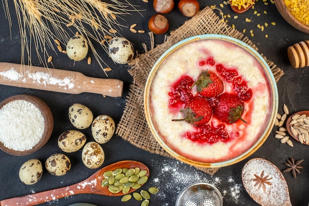 Close up view of delicious breakfast served with strawberries jam in a bowl and flour hazelnuts eggs spoons on dark color background