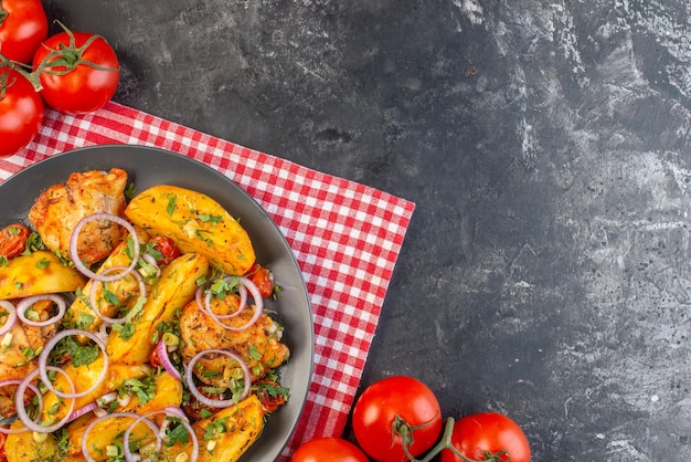 Close up view of delicious chicken meal with potatoes and vegetables greens on folded red stripped towel tomatoes with stems on dark color background with free space