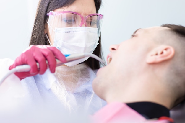 Close up view of female dentist in protective mask and glasses examines a male patient.