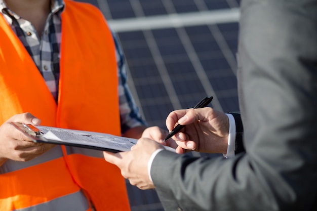 Close up view on foreman and client sigining contract at solar power station.