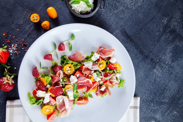 Close up view on fresh, summer salad with cherry tomato, strawberry, jamon and microgreen. Tasty food flat lay. Food for healthy and delicious lunch. Copy space. Top view