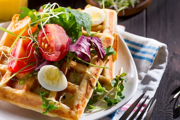 Close up view of freshly cooked healthy breakfast with homemade waffles, tomatoes and cut egg on a plate