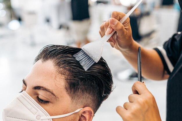 Close up view of a hairdresser colouring the hair of a man with a mask lying on a chair in a salon