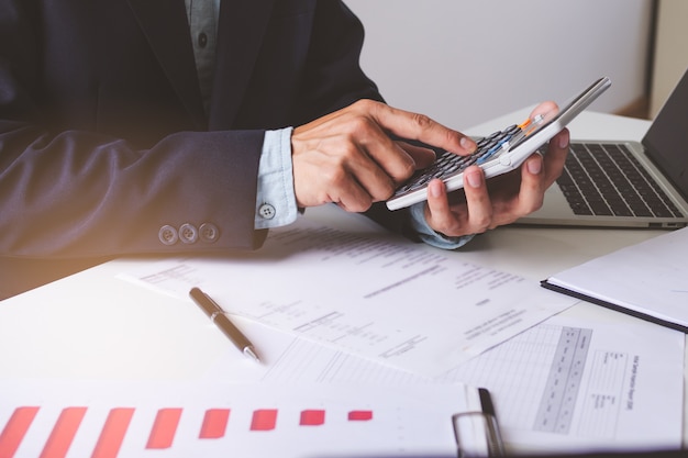 Close up view hands of businessman using calculator and doing accounting with graph and documents on the table.