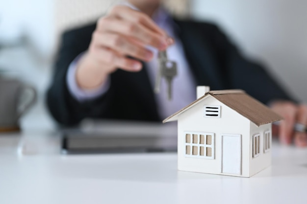 Close up view house model on white table and businessman holding keys in background Real estate moving home or renting property