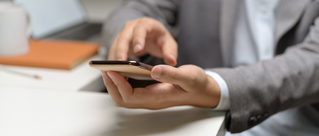 Close up view of male hands using smartphone while sitting at white office desk