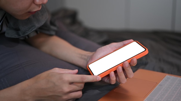 Close up view man laying on comfortable bed and using smart phone at night