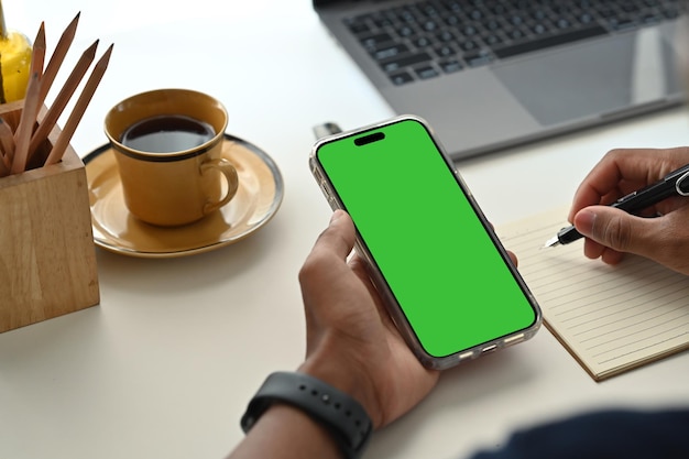 Close up view of man worker sitting at working desk and using smart phone Green empty screen for your advertise design