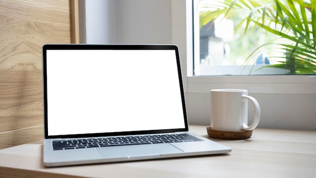 Close up view mock up laptop and coffee cup on wooden desk in living room