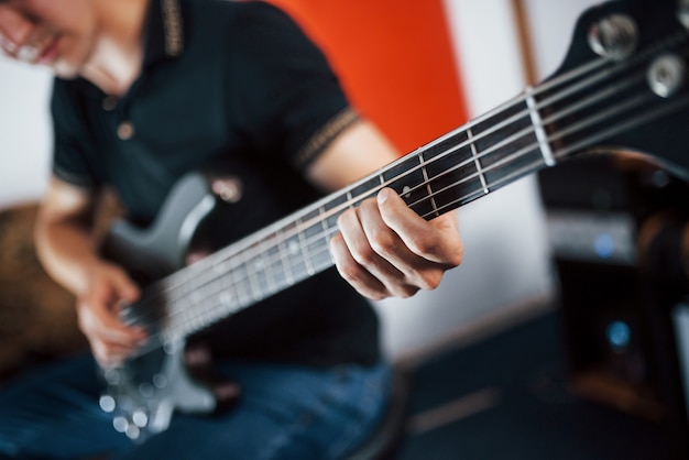 Close up view of musician plays bass guitar indoors.