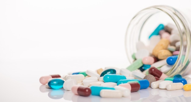 Close up view photo image of glass jar and pouring out different colorful multicolored capsules isolated white background